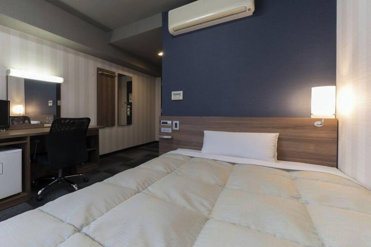 Een hotelkamer met een bed, bureau, stoel en een airconditioning.