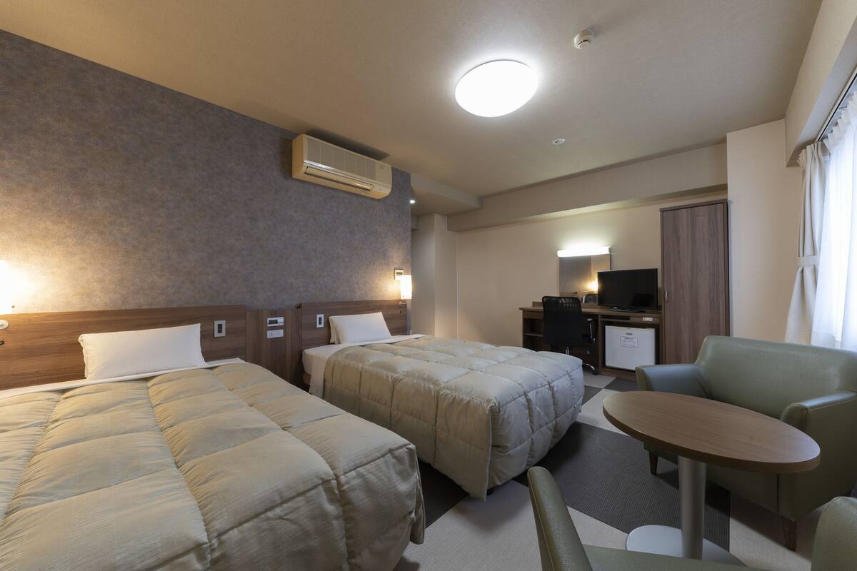 Een hotelkamer met twee bedden, een bureau, een stoel en een televisie.
