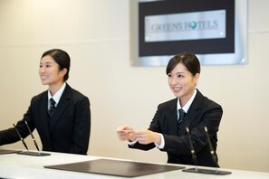Two individuals in business attire at a conference table with microphones, in a room with a sign reading "GREENSHOTELS". - Hotel Econo Tsu Station (Tsu)