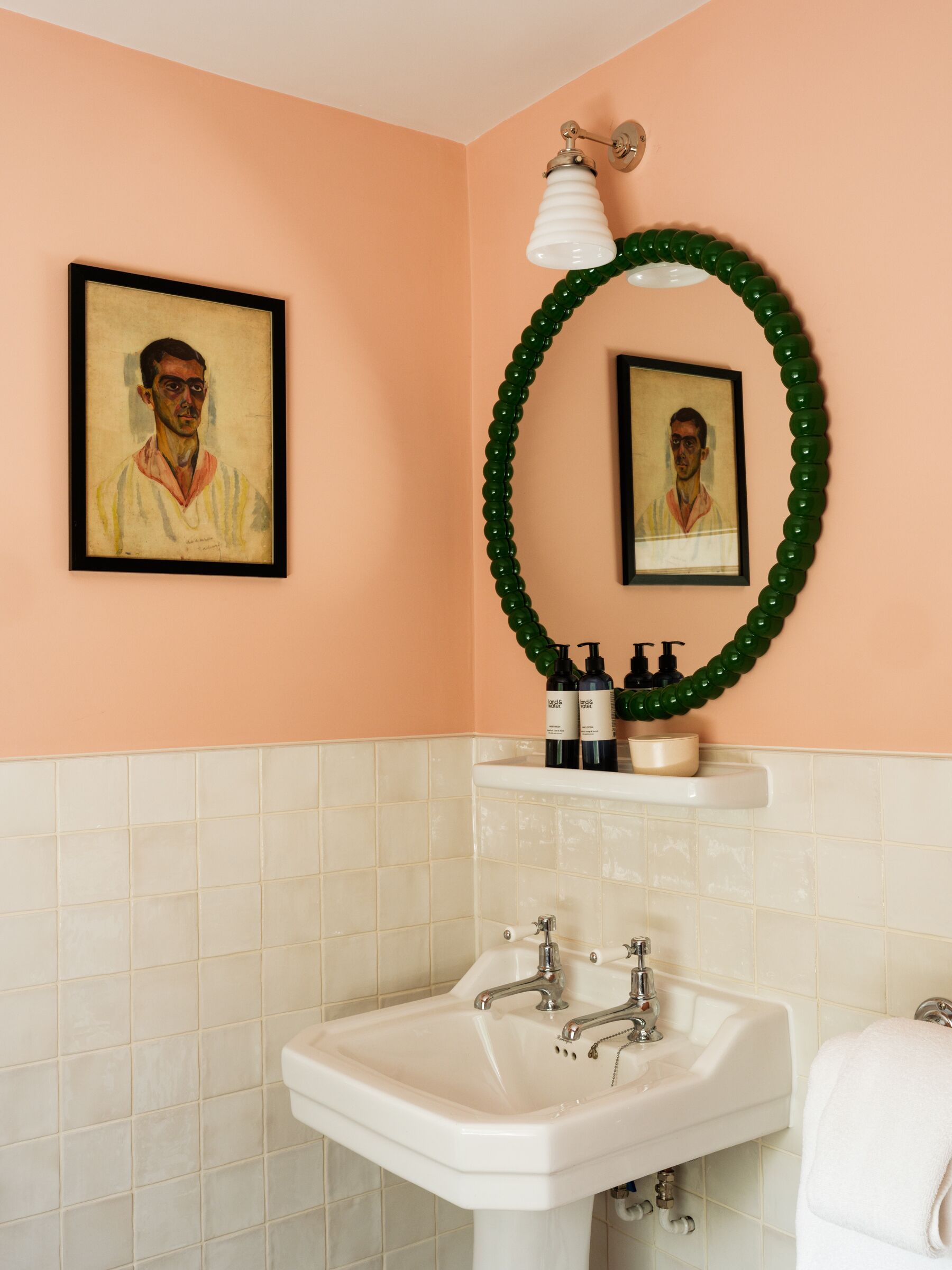 Ein Badezimmer mit Waschbecken, Spiegel, einem gerahmten Kunstwerk und einem grünen Dekowreath.