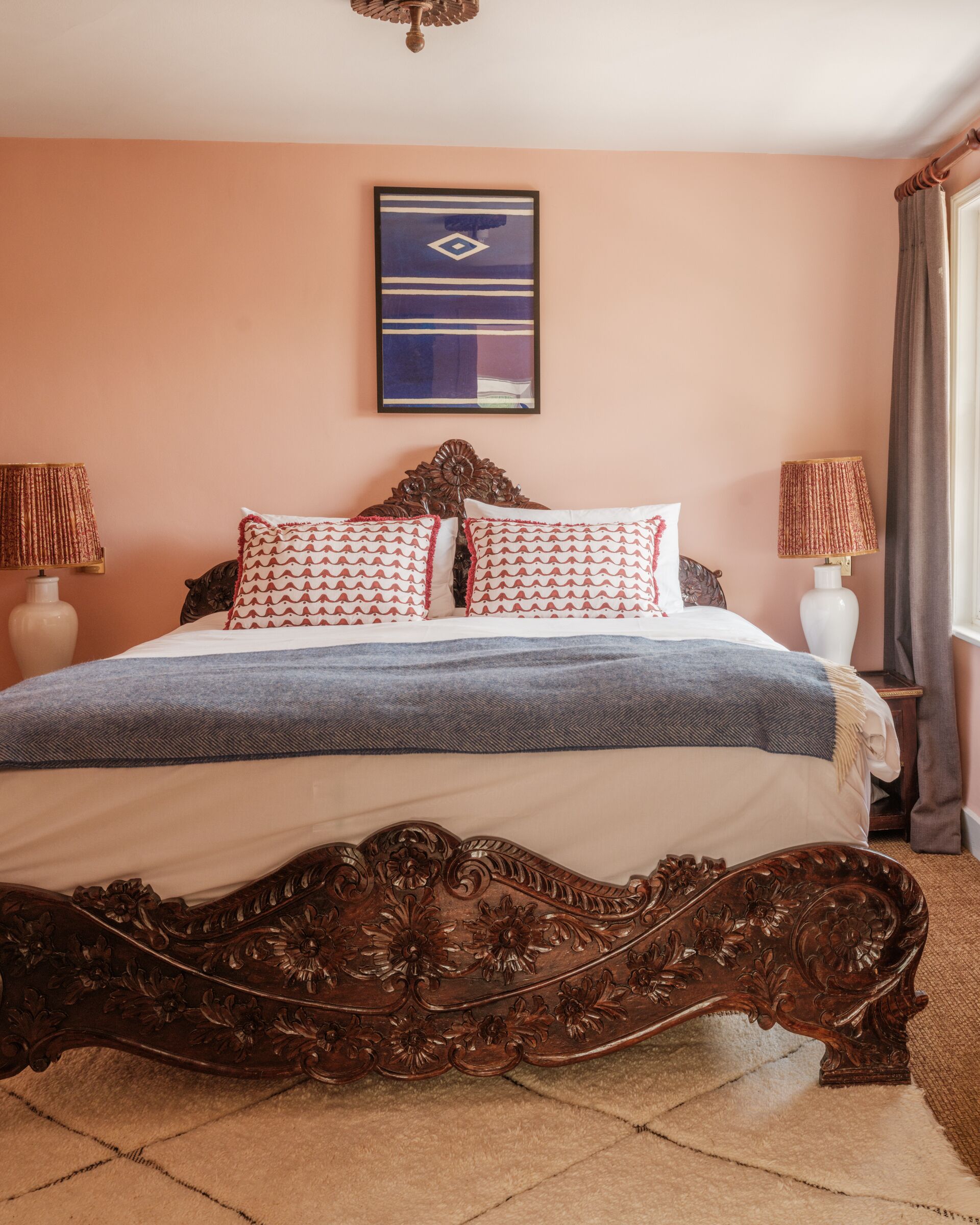 A bedroom with a large bed, two bedside lamps, a decorative headboard, and a framed artwork on the wall.