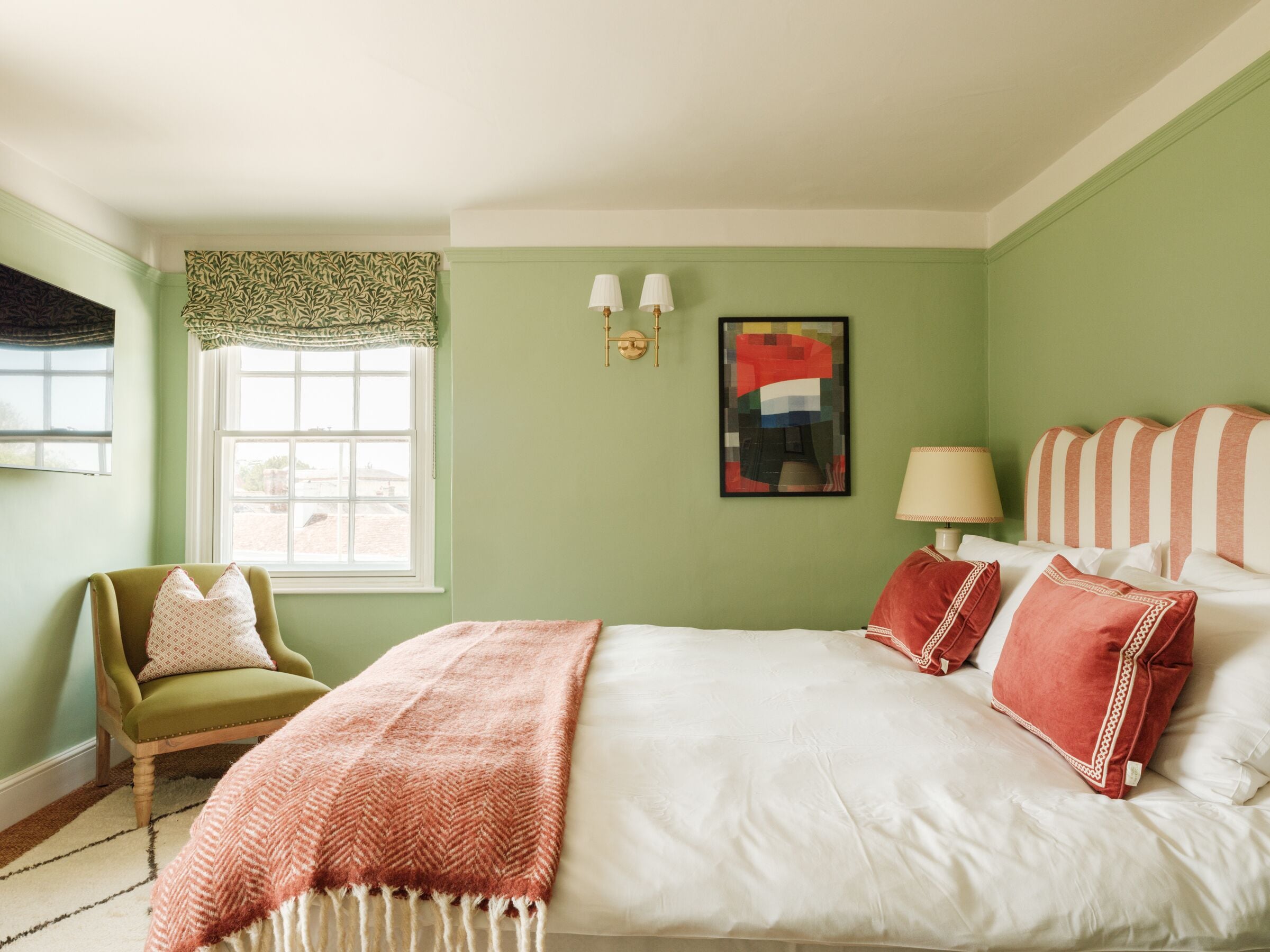 Un dormitorio con cama, una silla, un ventanal y una lámpara de pared.