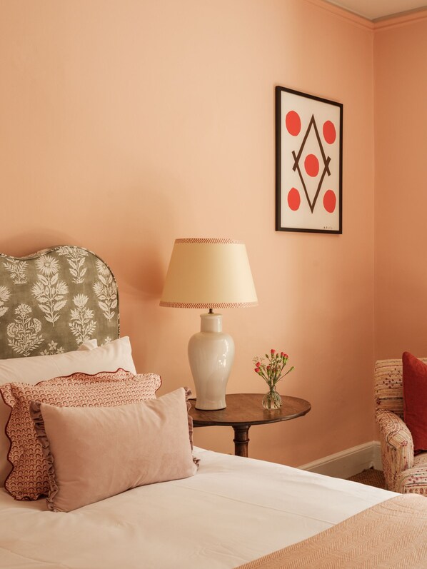 A neatly arranged bedroom with a bed, pillows, a bedside table with a lamp, a framed artwork, and a chair. - The Pembroke Arms (Salisbury)
