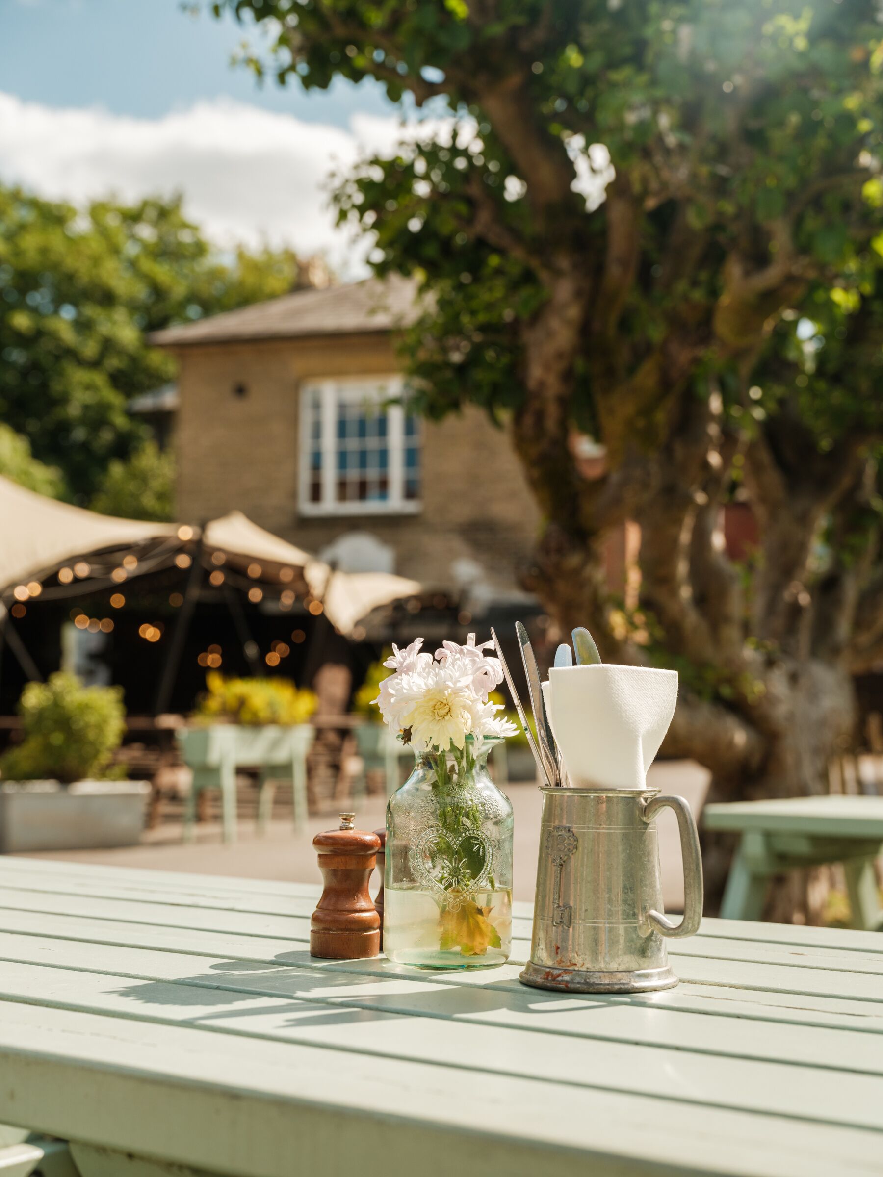 A table with a vase of flowers, a sugar bowl, and a metal pitcher.