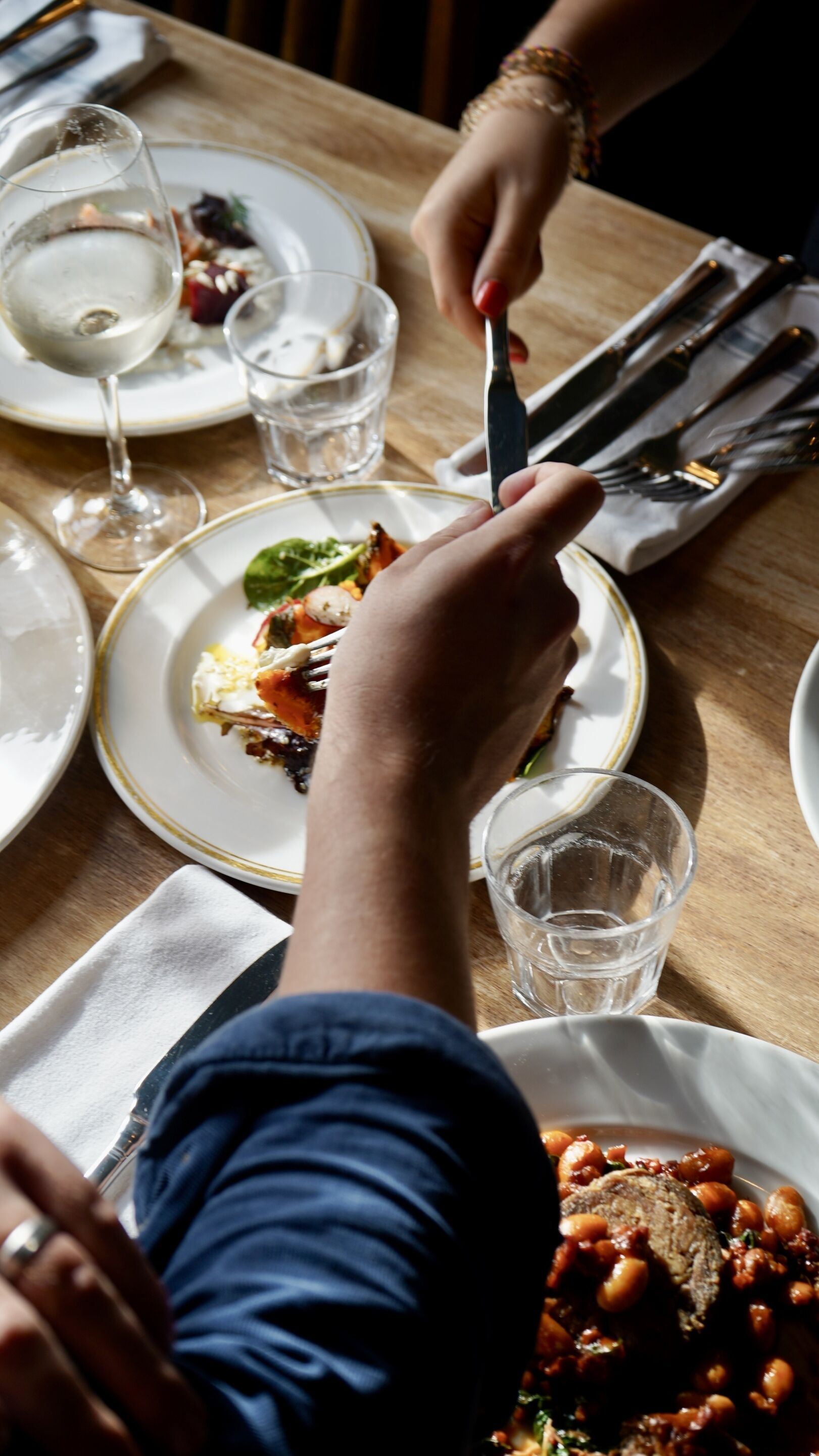 A dining table with plates of food, glasses, and cutlery.