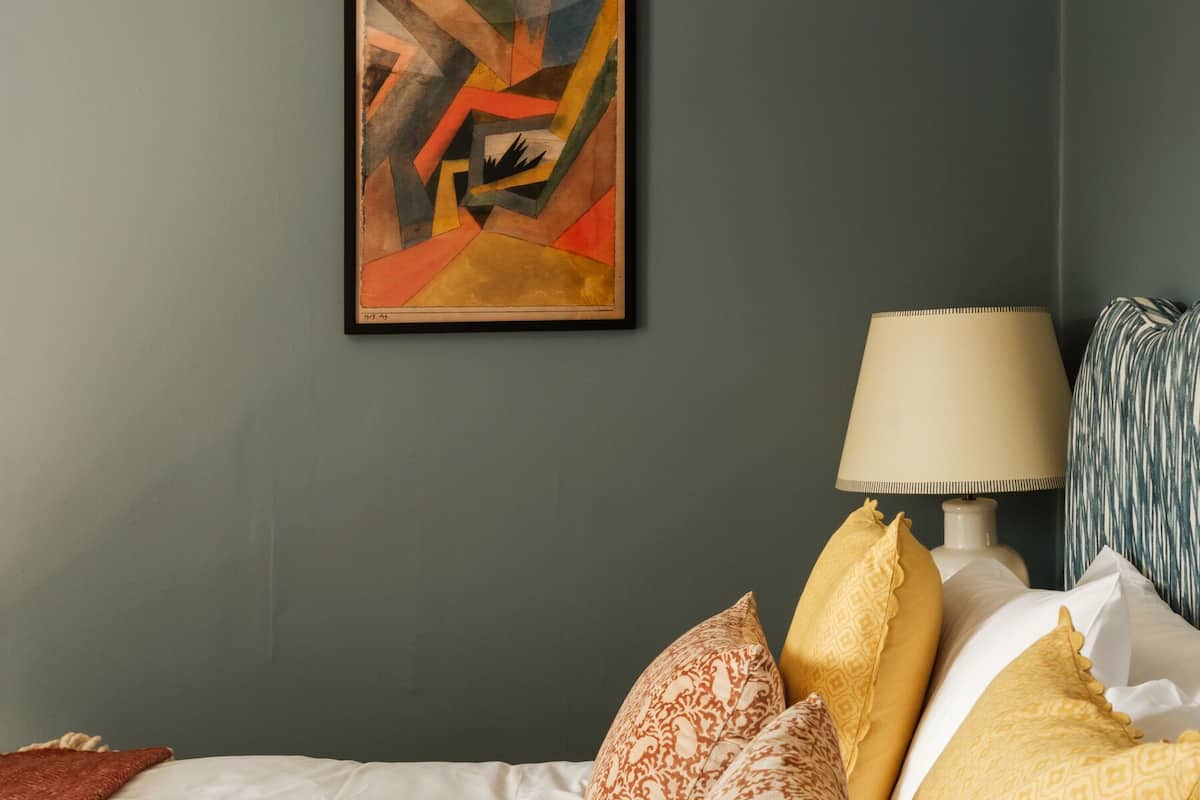 A bedroom with a bed, pillows, a lamp, and a painting on the wall.
