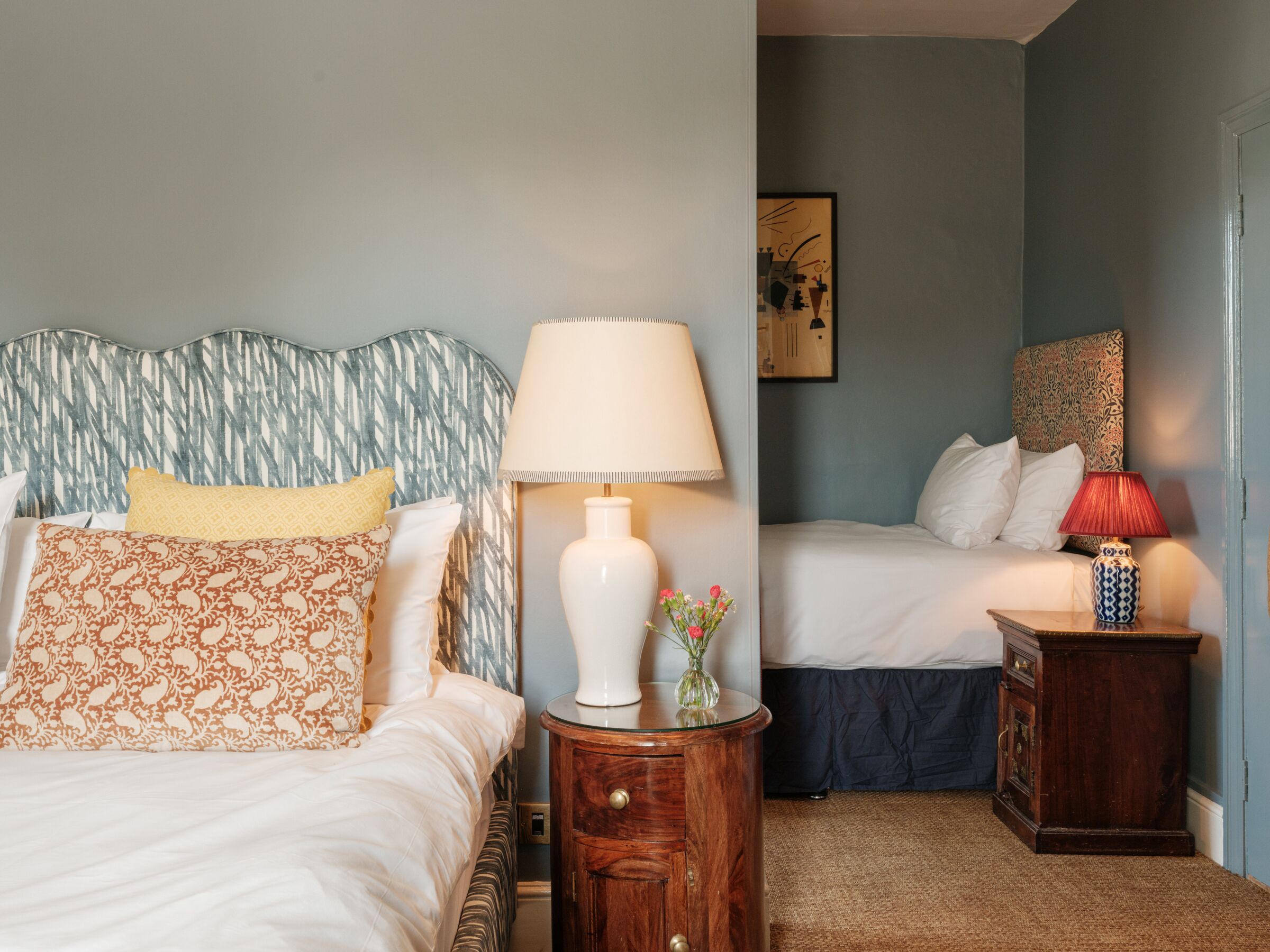 Un dormitorio con dos camas, una mesita de noche con lámpara y una pequeña mesa con un florero.