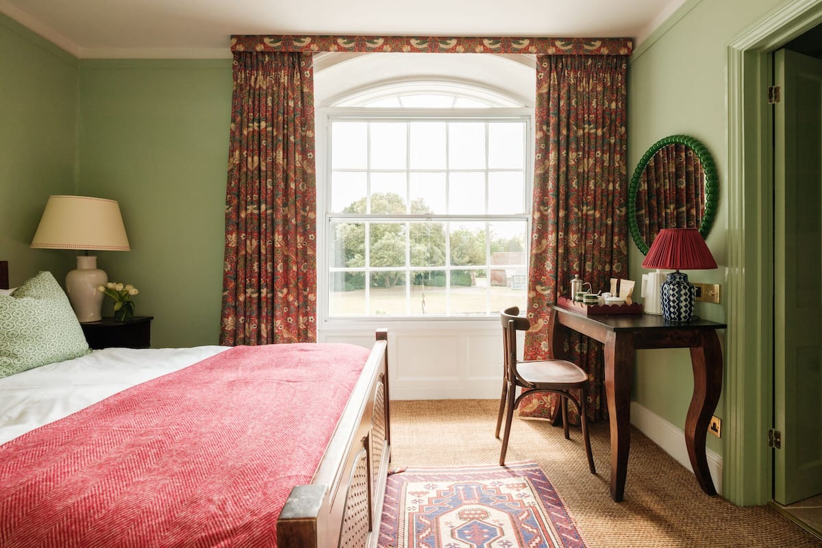 A bedroom with a bed, a chair, a desk, and a window with curtains.