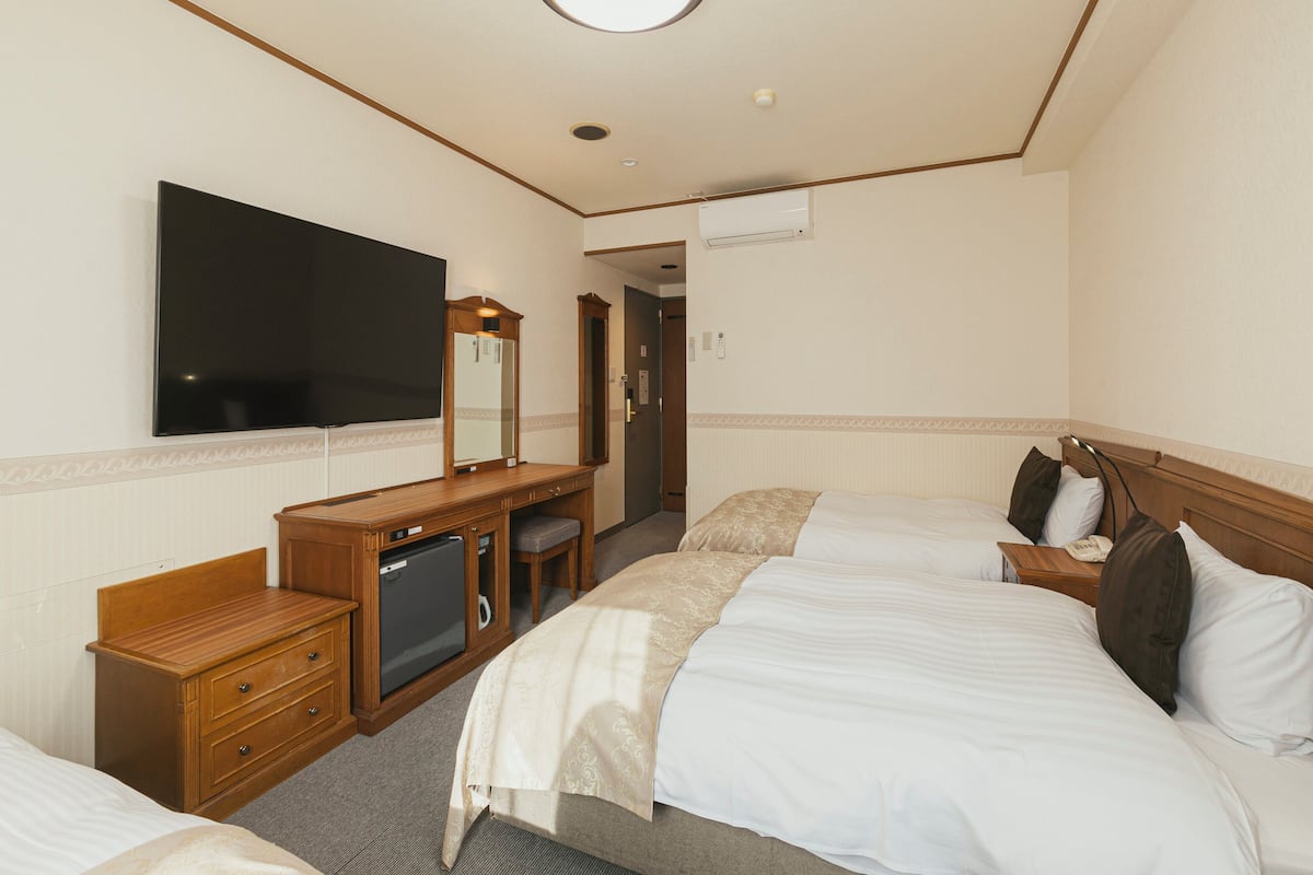 A hotel room with two beds, a TV, a dresser, and a mirror.
