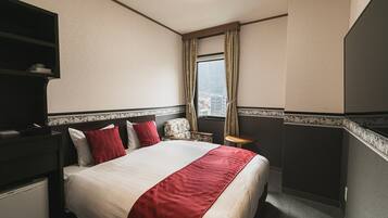 Habitación de hotel con cama, escritorio, silla, ventana con cortinas y vistas a la ciudad.