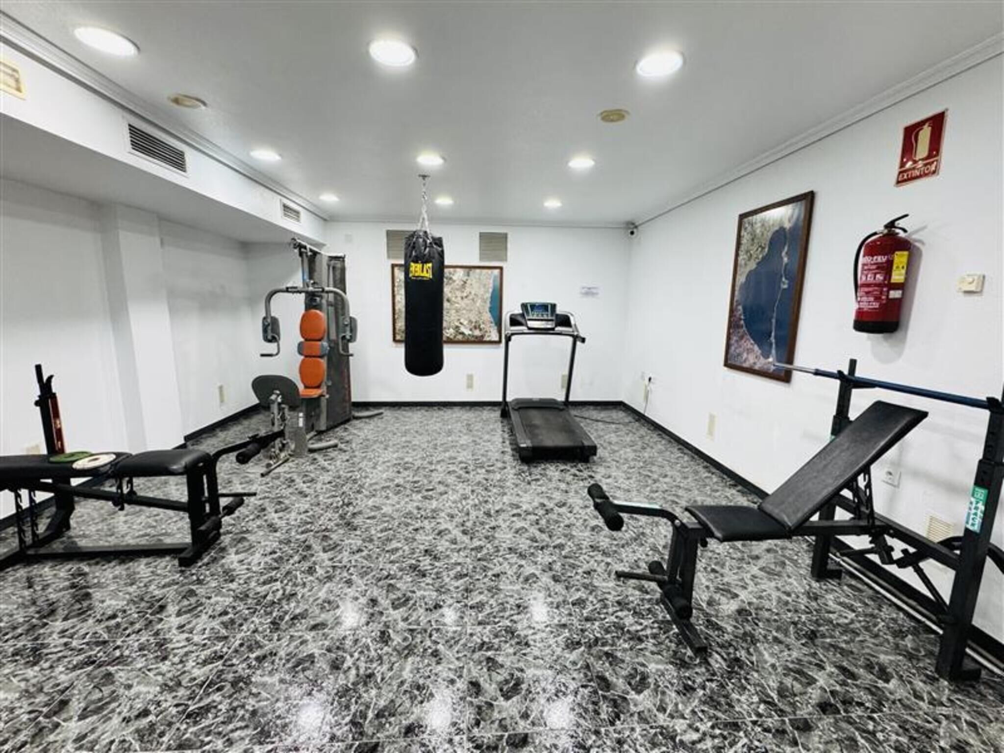 Un gimnasio con un saco de boxeo, cintas de correr y máquinas de pesas.