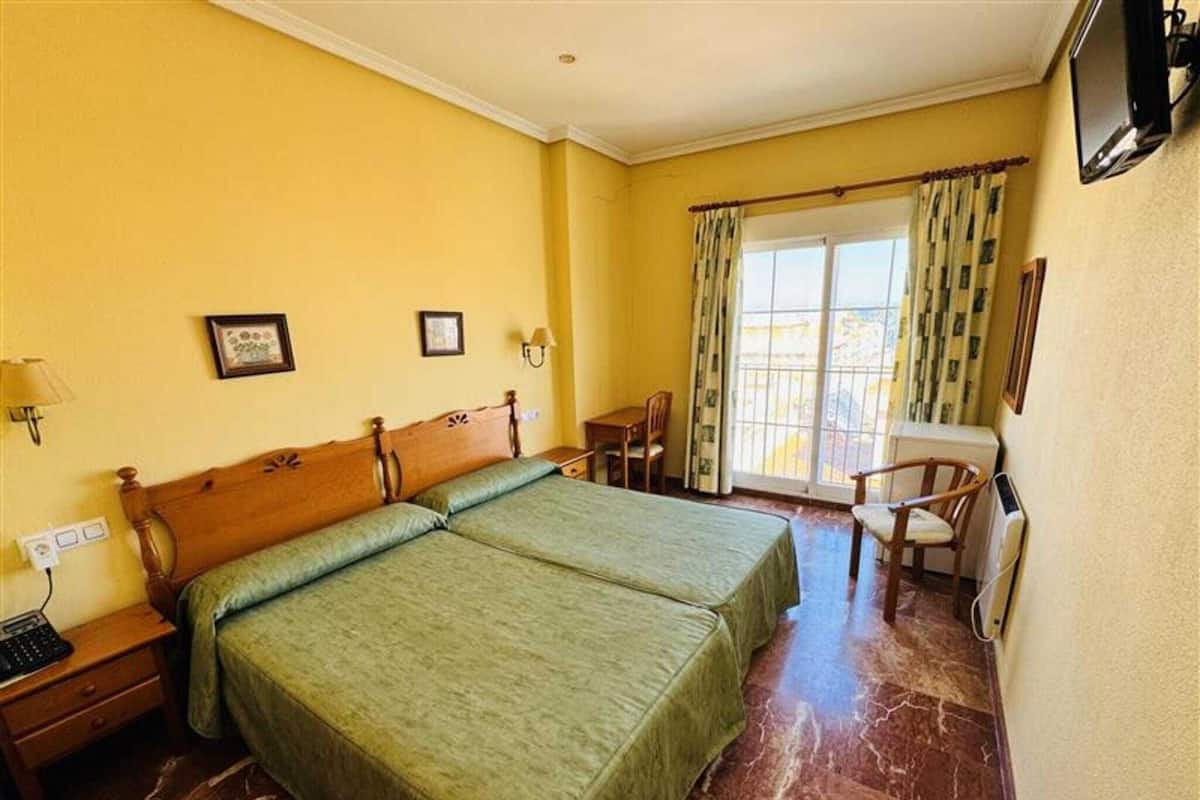 Habitación de hotel con dos camas, un escritorio, una silla, un televisor y una ventana con cortinas.