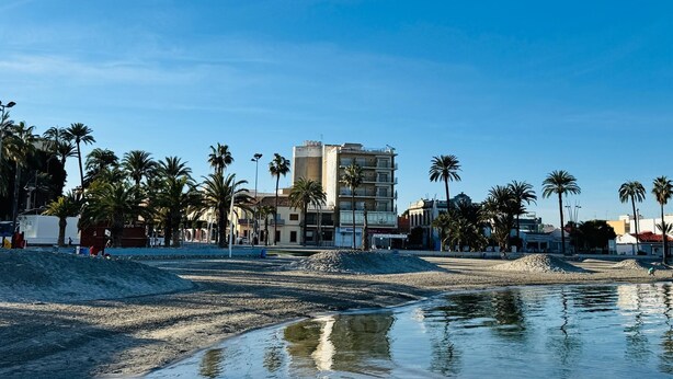 A beach with palm trees, a building, and a calm water body. - Albohera Playa hotel by Belvilla Resorts (San Javier)
