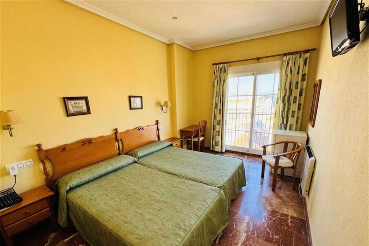 Une chambre d’hôtel avec deux lits, un bureau, une chaise, une télévision et une fenêtre avec des rideaux.
