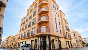 A multi-story hotel with a prominent 'Hotel Alboran' sign, a corner entrance, and a parking area with cars. - Albohera Playa hotel by Belvilla Resorts (San Javier)