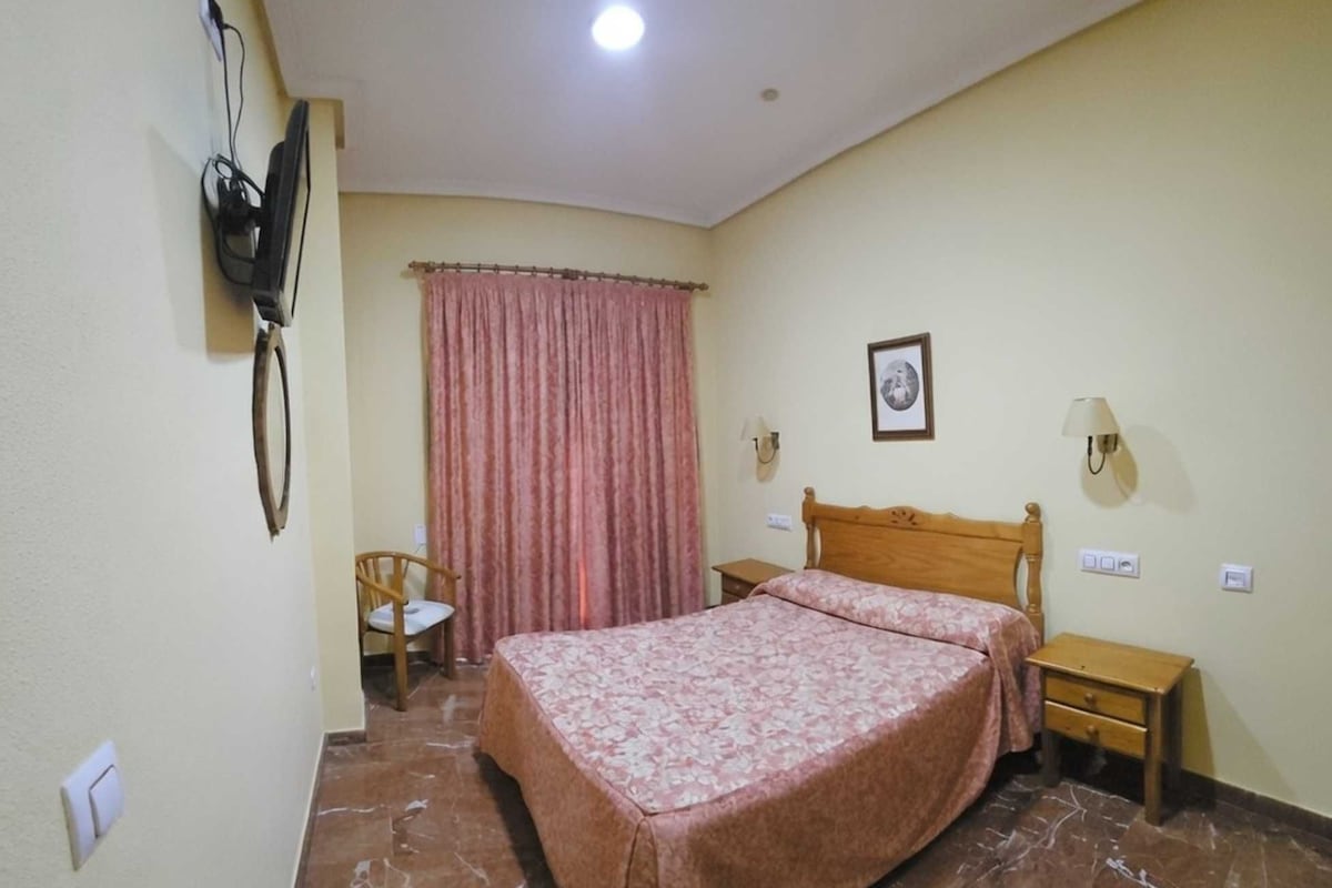 A hotel room with a bed, a chair, a desk, a lamp, and a picture on the wall.