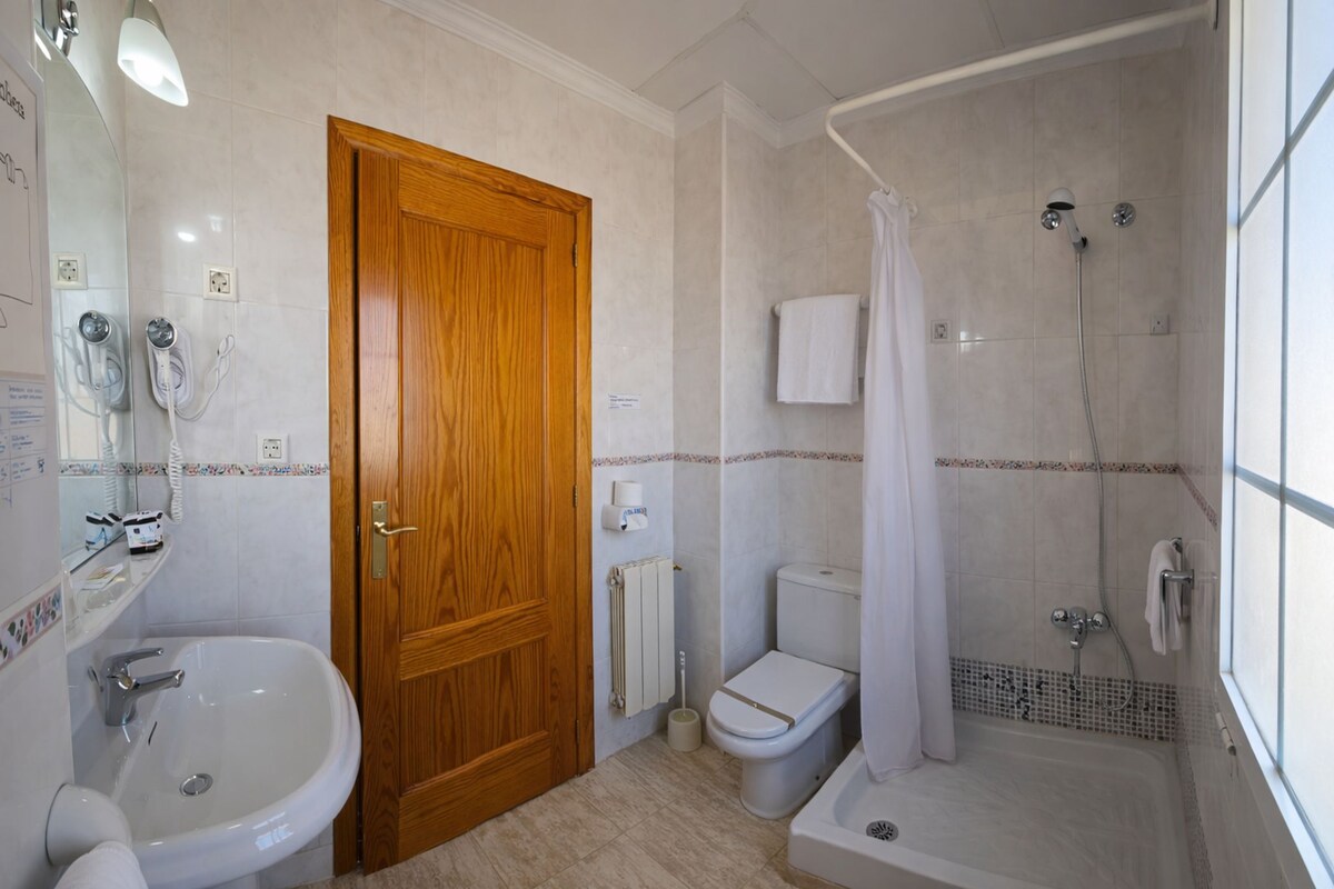 A bathroom with a wooden door, a sink, a toilet, and a shower area.
