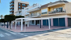 A multi-story building with balconies, a covered outdoor seating area, and a pedestrian crossing. - Albohera Playa hotel by Belvilla Resorts (San Javier)