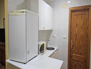 Egy konyha, amelyben hűtőszekrény, mikrohullámú sütő, mosogató és fa ajtó található.