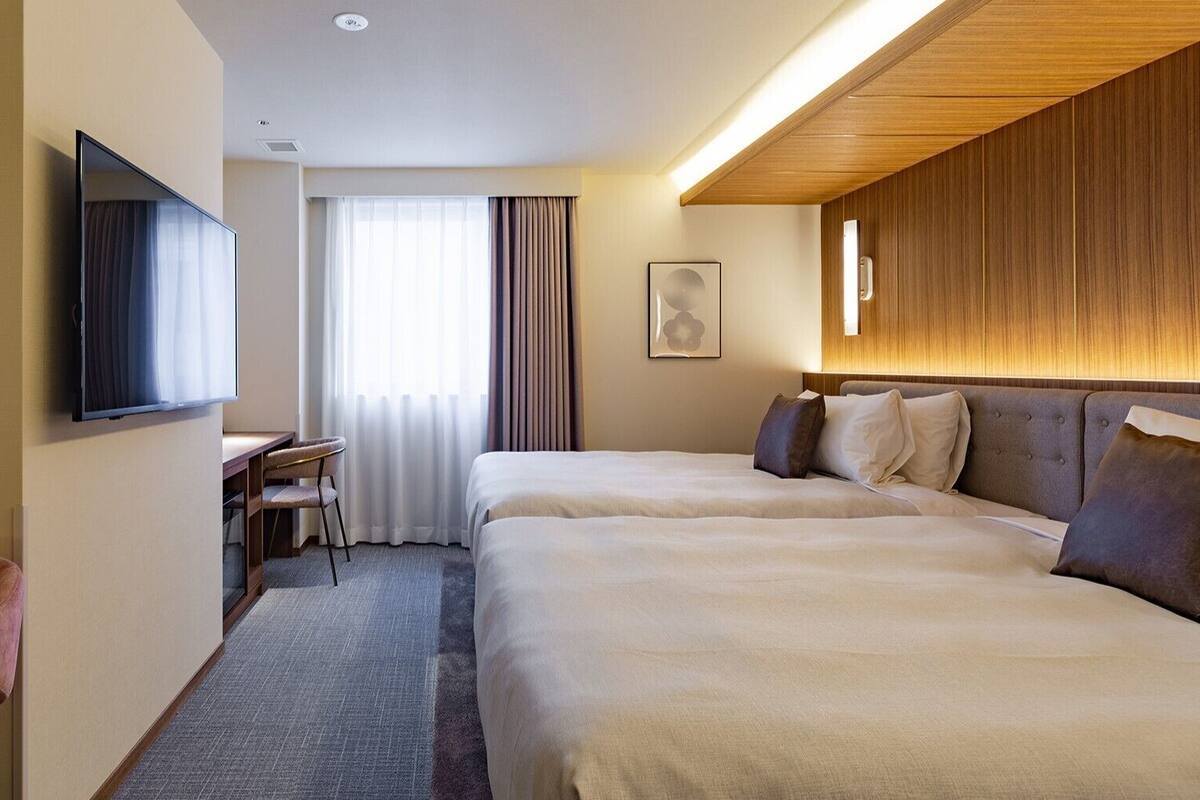 Una habitación de hotel con dos camas, un escritorio, una silla, un televisor y una ventana con cortinas.