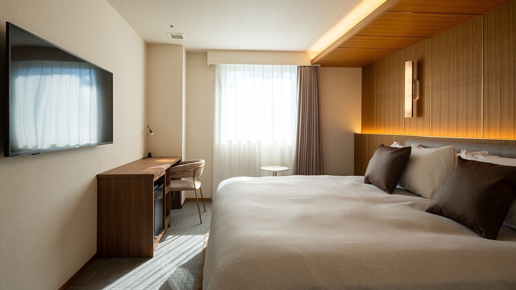 A hotel room with a bed, desk, chair, TV, and a small table.