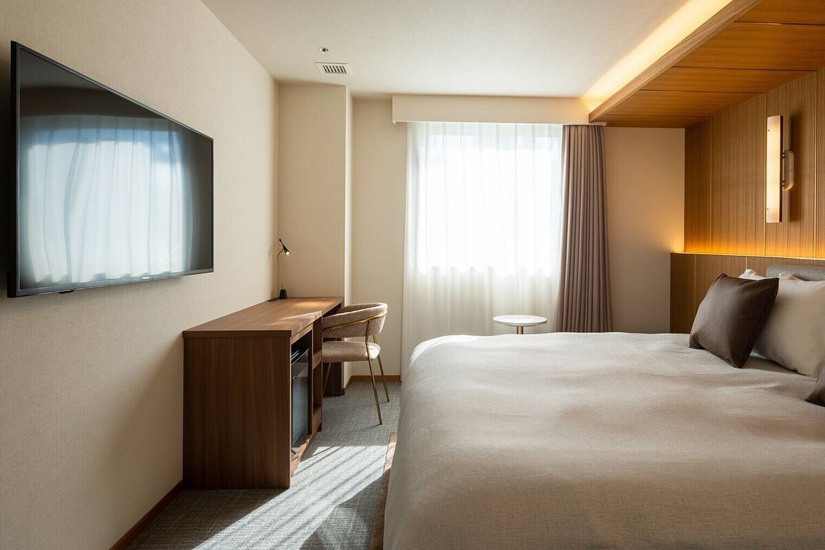 Habitación de hotel con cama, escritorio, silla, televisor y una mesita.