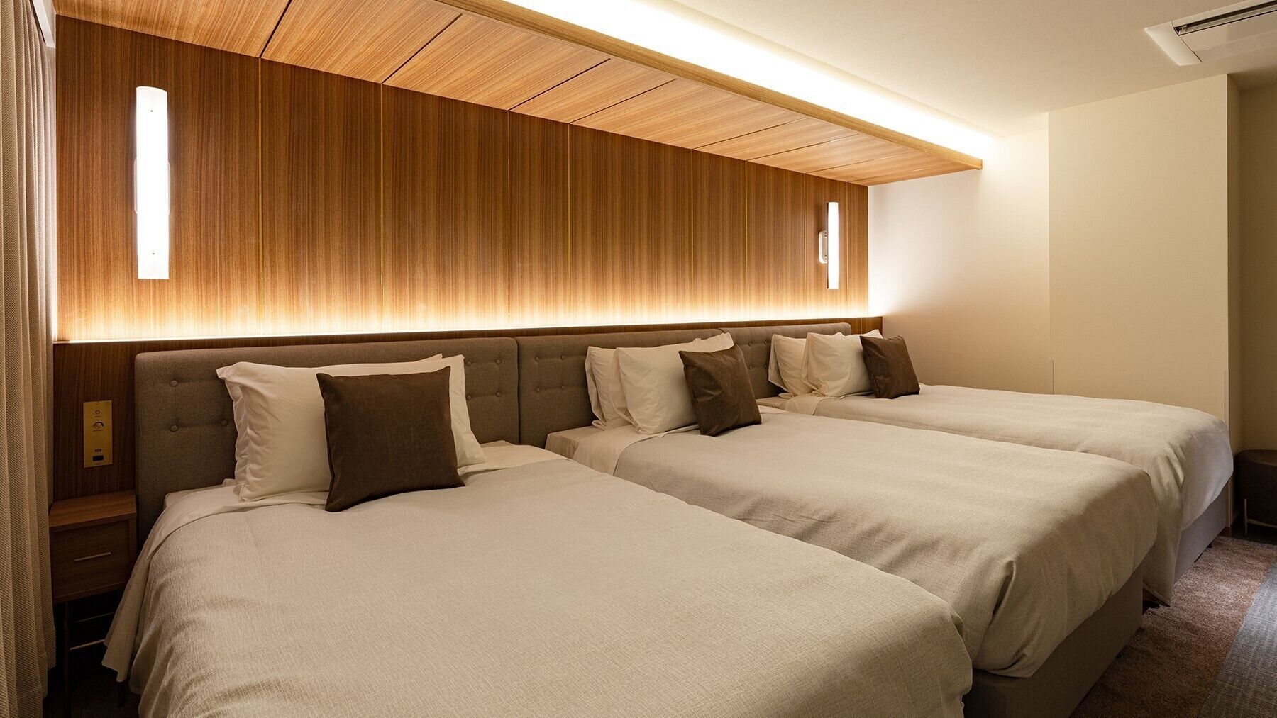 A hotel room with two beds, a wooden headboard, a wall-mounted air conditioner, and a bedside table.