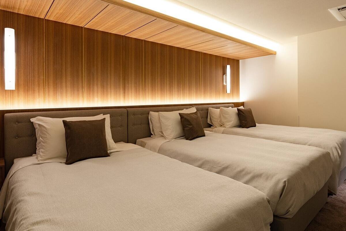 Una habitación de hotel con dos camas, cabecero de madera, aire acondicionado de pared y mesita de noche.