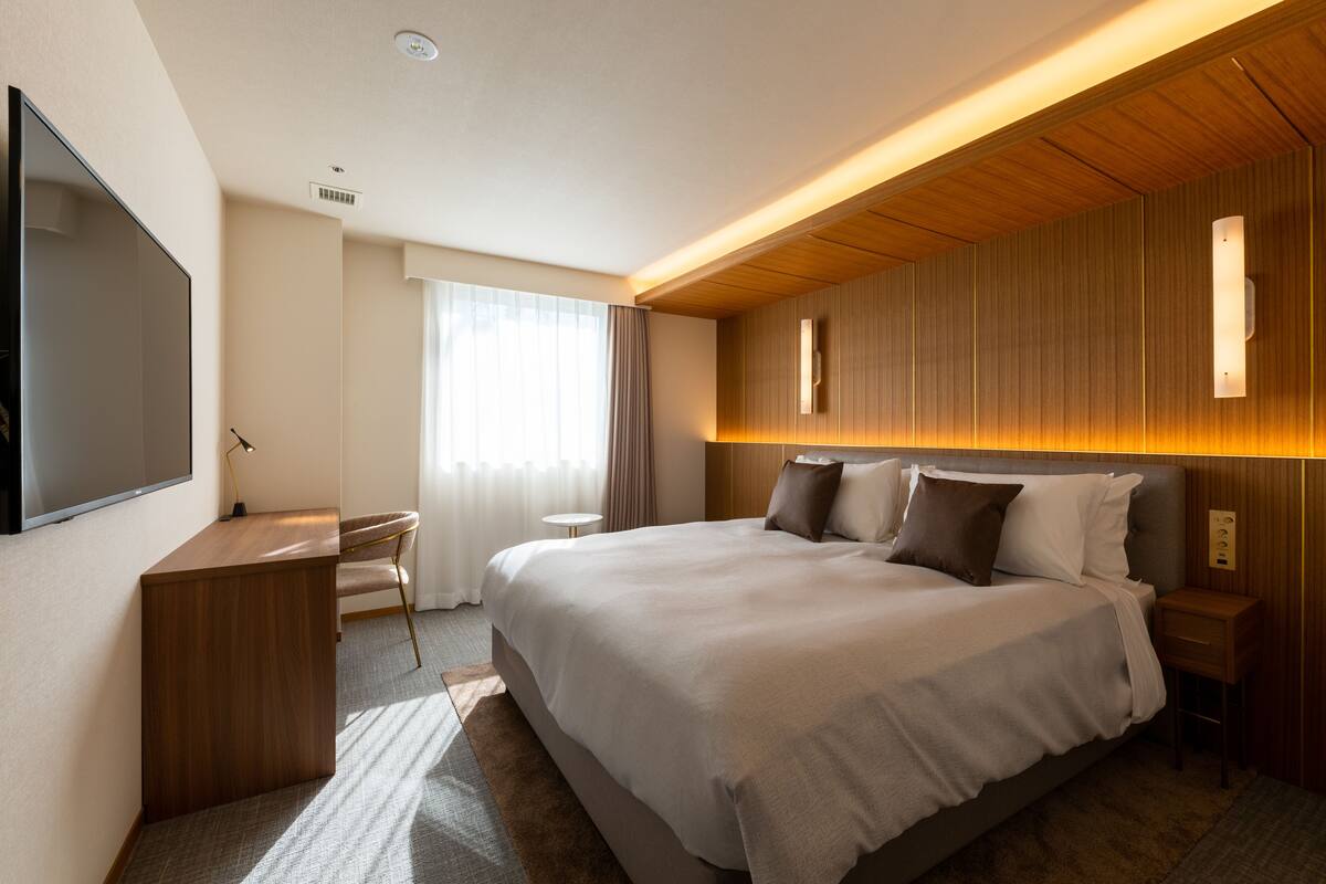 Una habitación de hotel moderna con una cama grande, un escritorio y un televisor de pantalla plana.