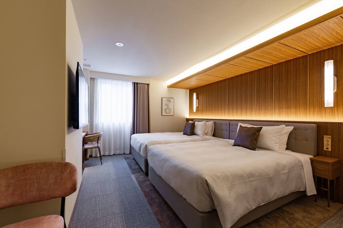 Una habitación de hotel con dos camas, un escritorio, una silla y un televisor.