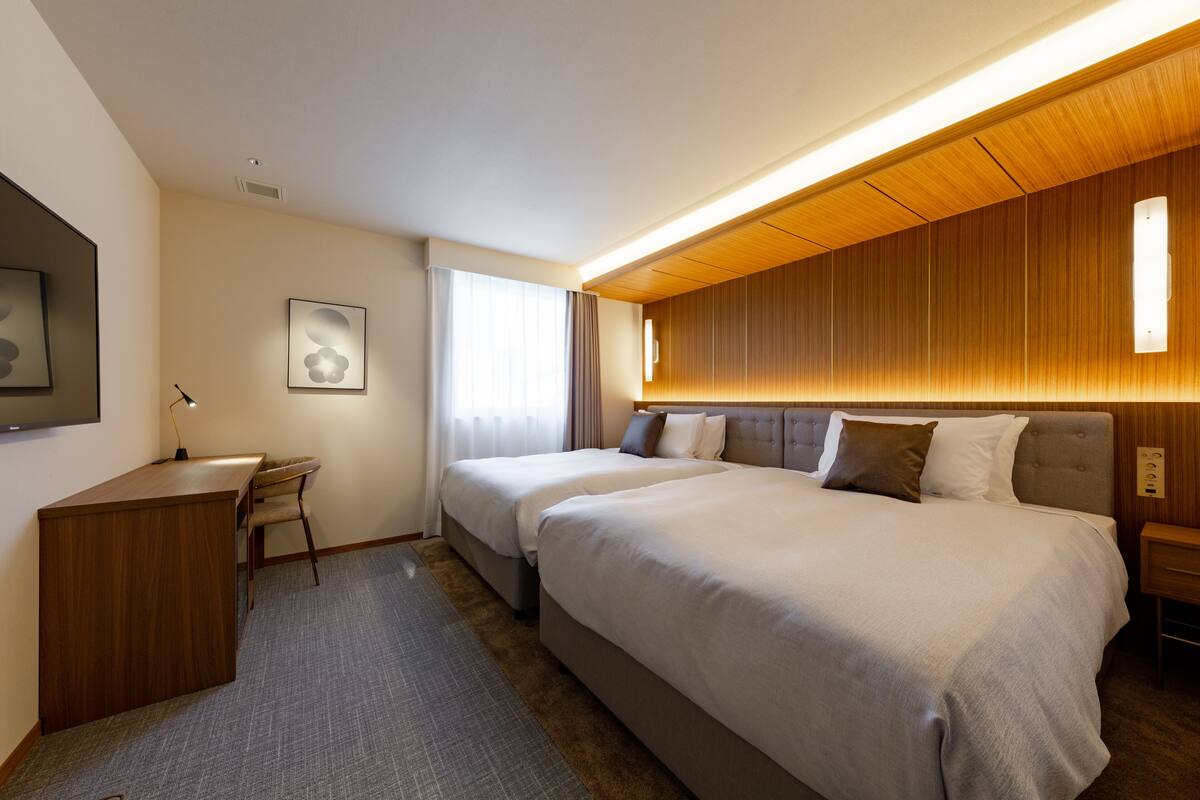 Una habitación de hotel con una cama grande, un escritorio y una silla. Hay una ventana con cortinas y una lámpara de pared.