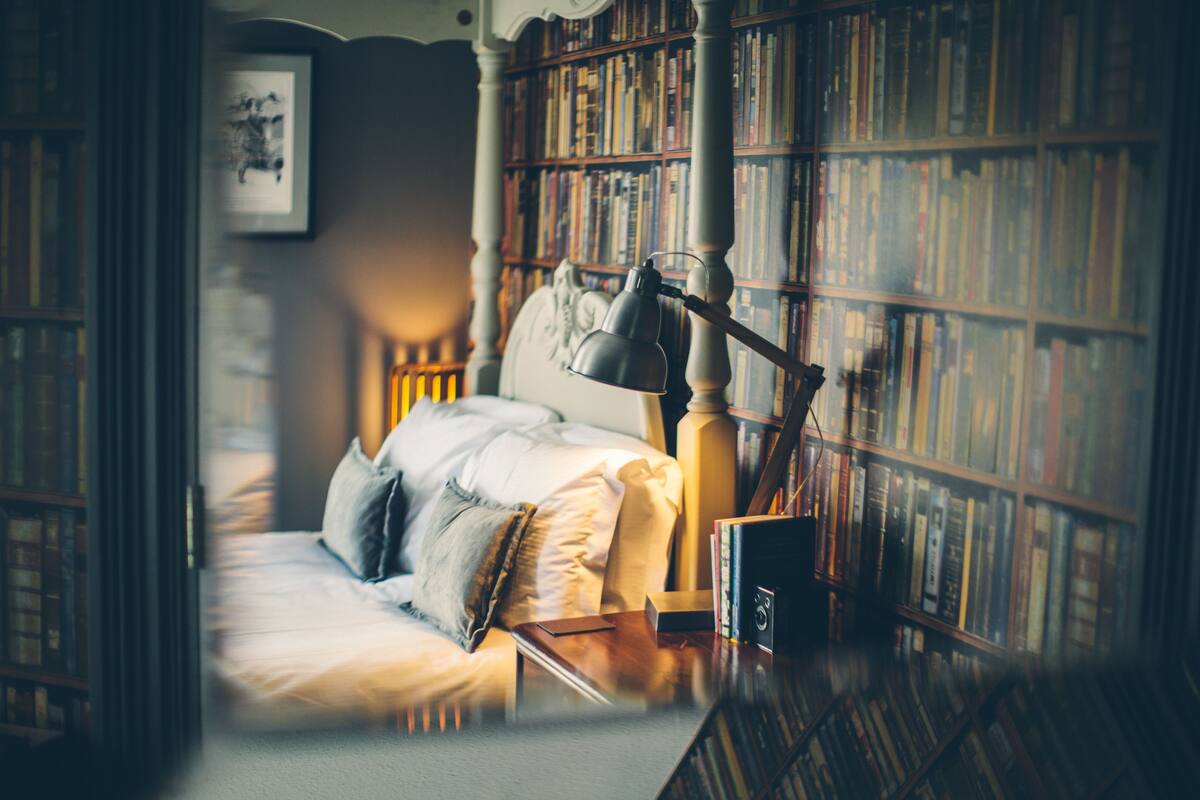 A cozy bedroom with a bed, a nightstand, and a bookshelf filled with books.