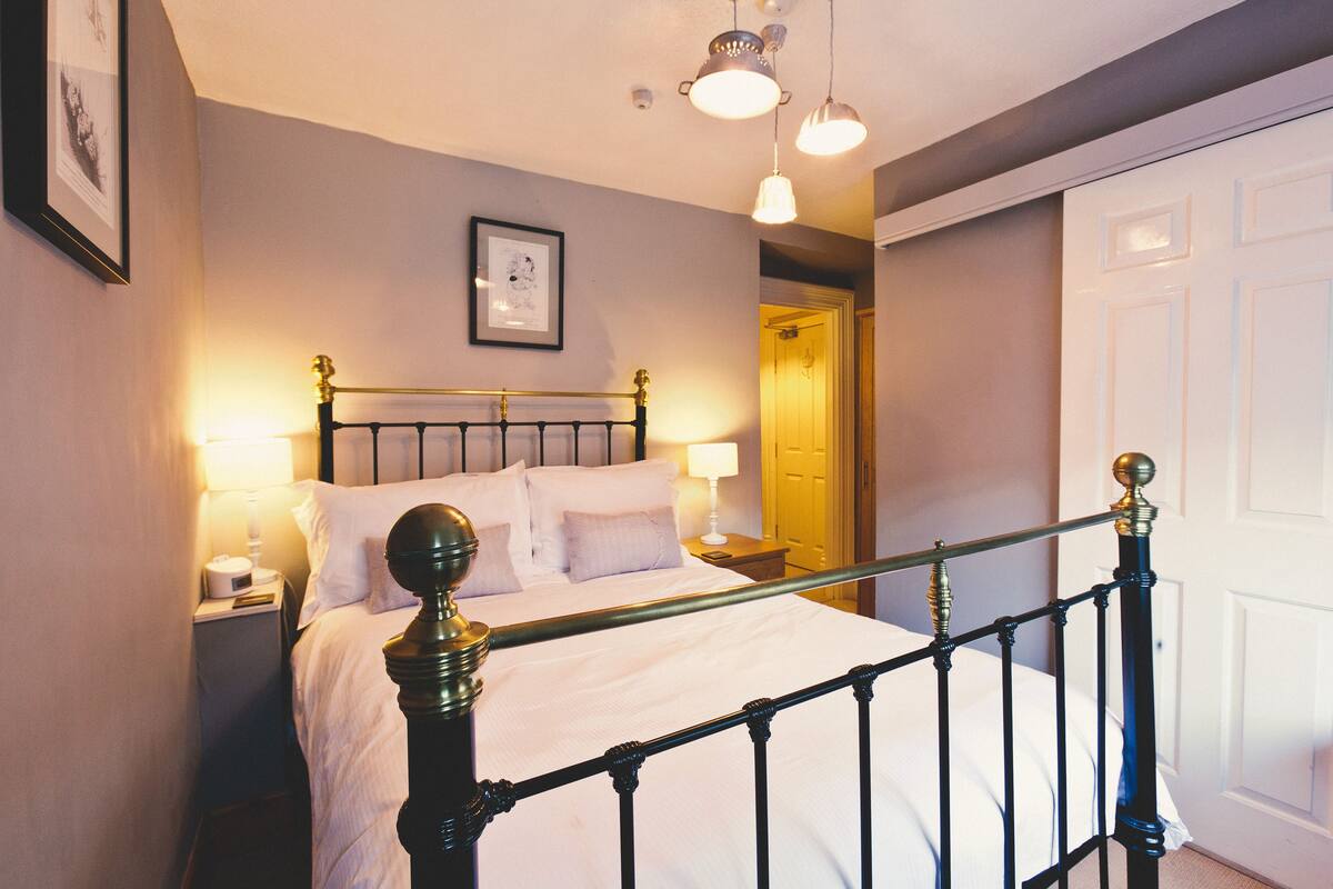 A neatly made bed with a black metal frame and white bedding, a bedside table with a lamp, and a framed picture on the wall.