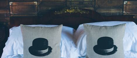 A bed with two pillows featuring a black hat design, set against a backdrop of stacked wooden suitcases.