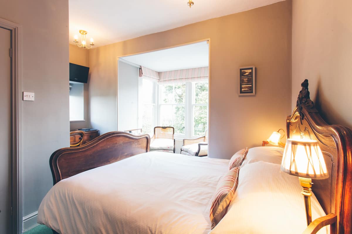 A bedroom with a large bed, a bedside lamp, a chair, and a window with curtains.