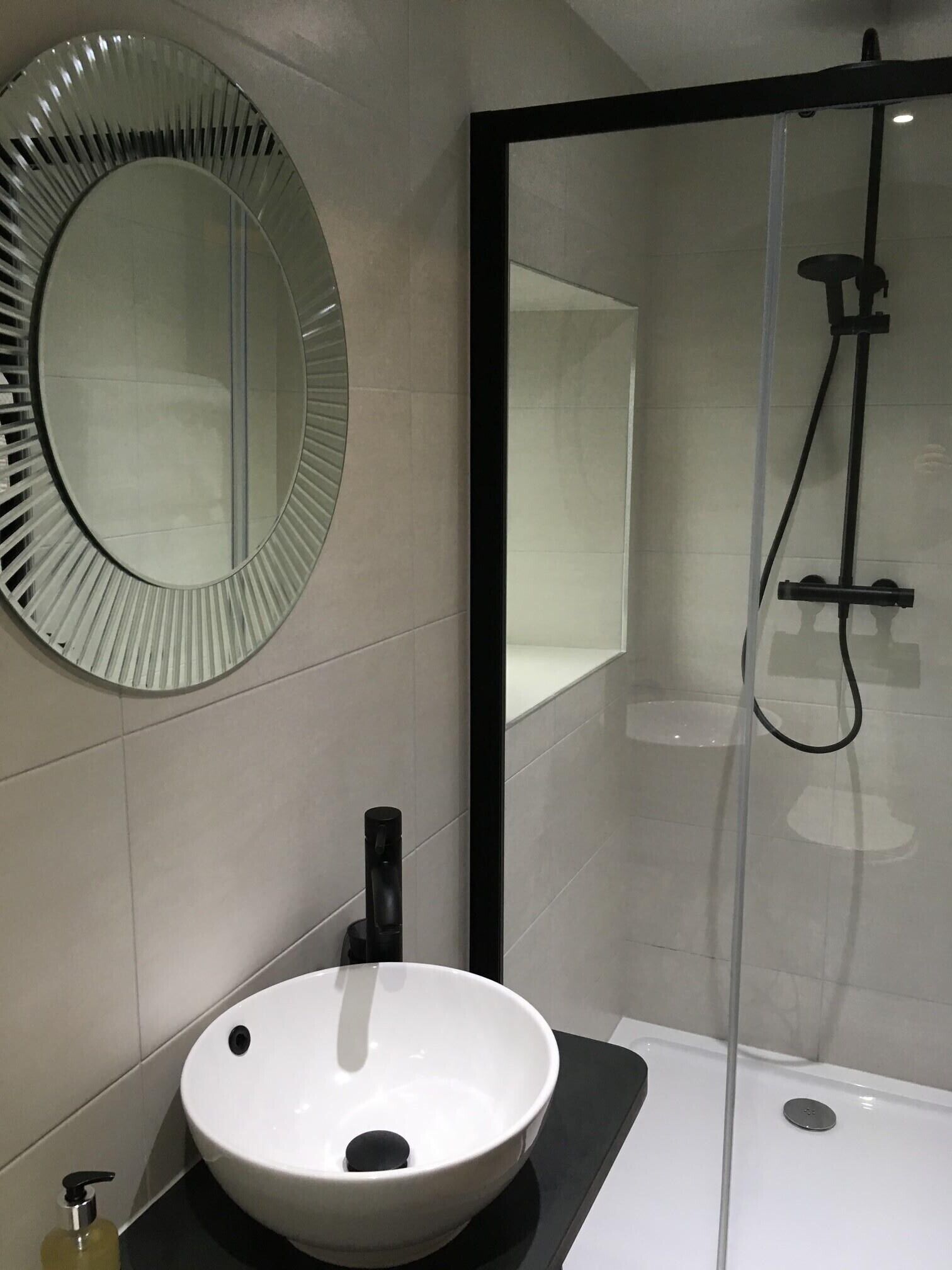 A bathroom with a round mirror, a white sink, and a glass-enclosed shower.