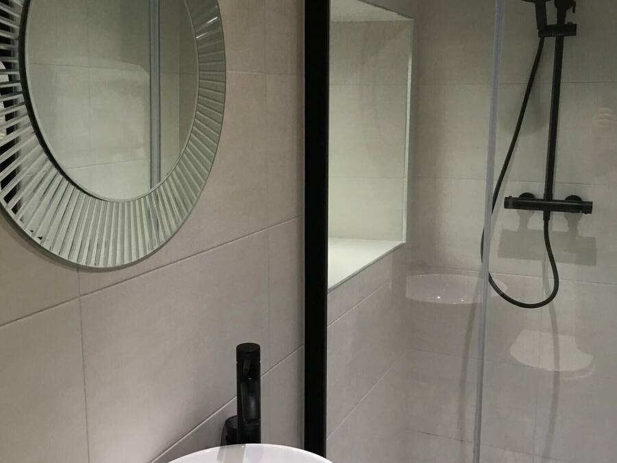 A bathroom with a round mirror, a white sink, and a glass-enclosed shower.