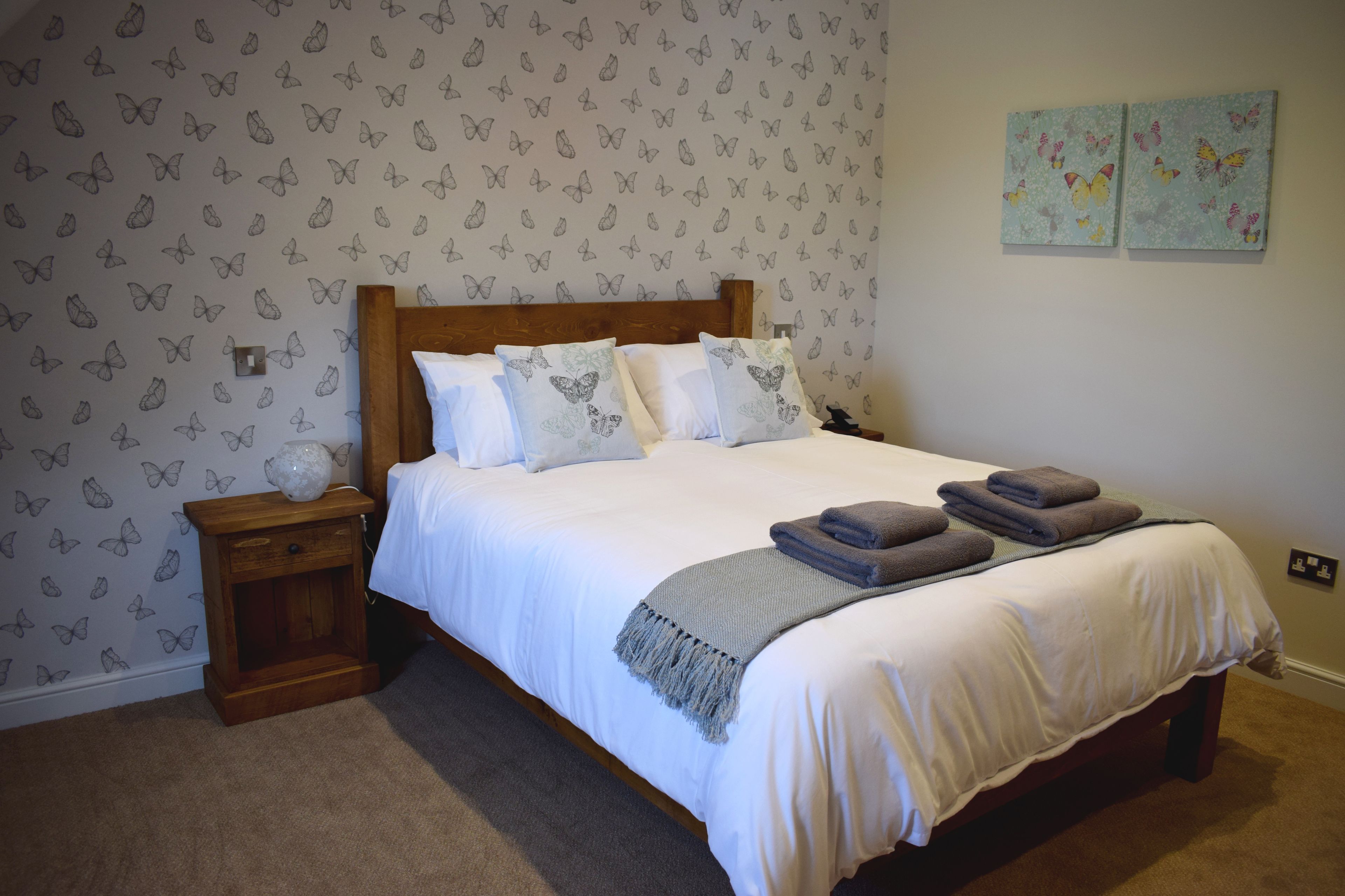 Una camera da letto con una testiera in legno, biancheria da letto bianca, un comodino con una lampada e carta da parati a motivi di farfalle.