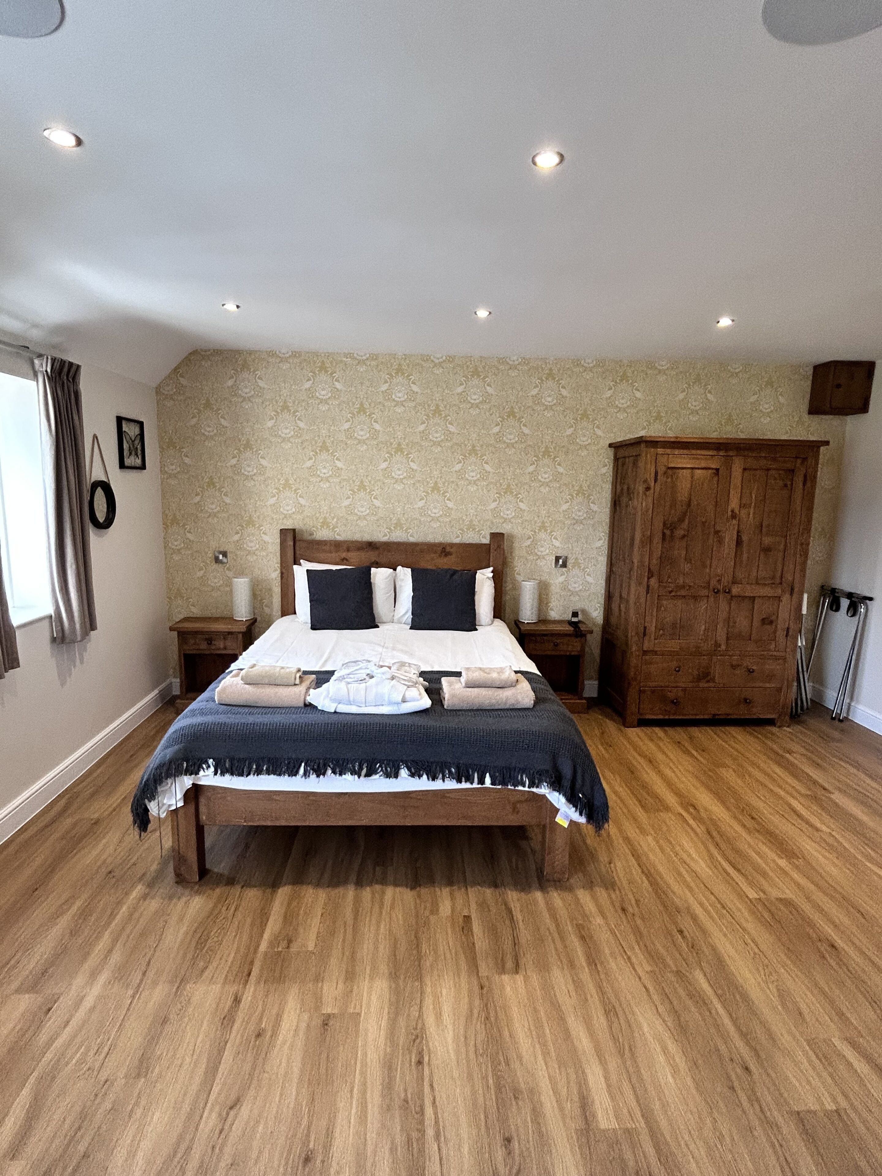 A bedroom with a wooden bed, a wooden wardrobe, and a patterned wallpaper.