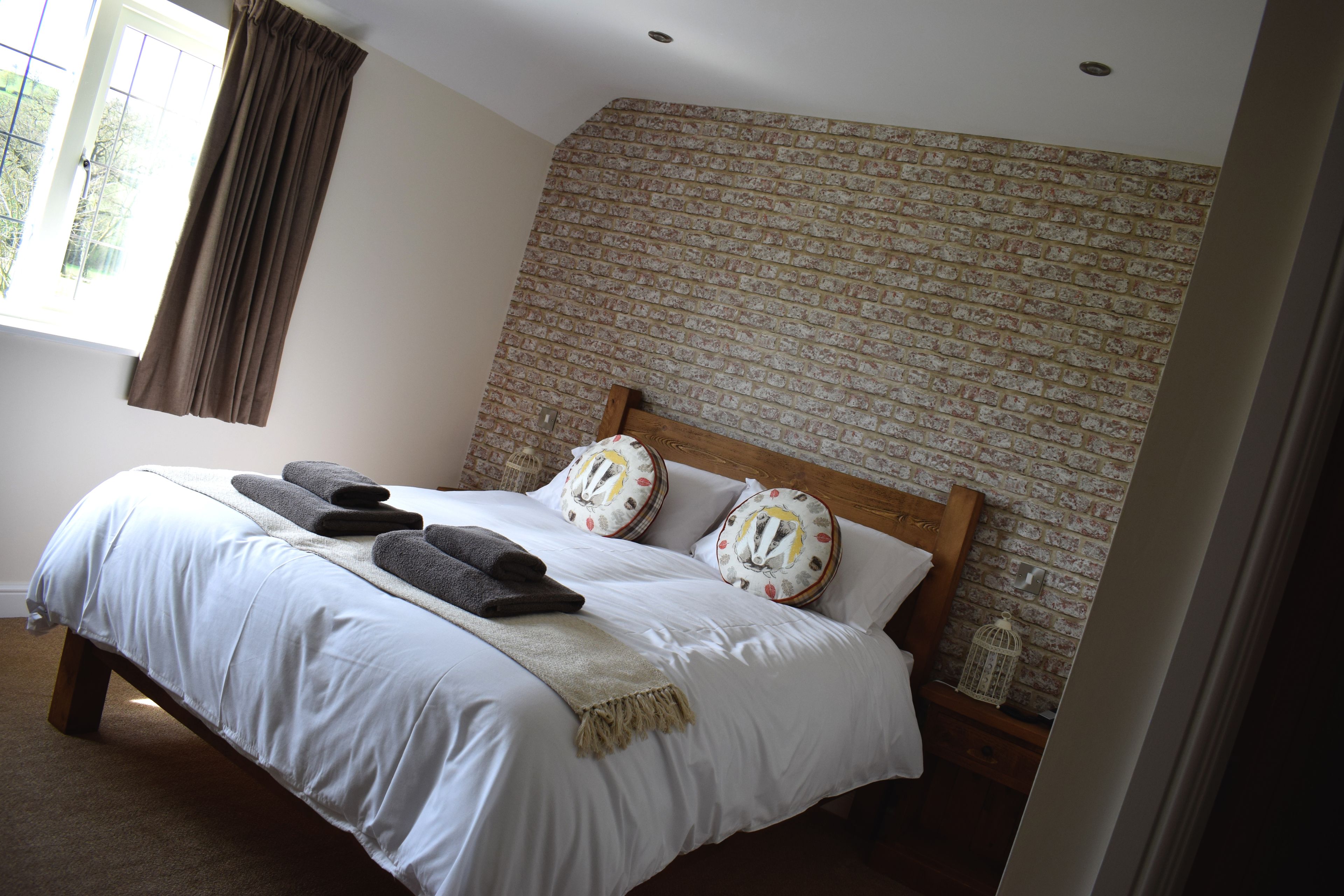 Una cama bien hecha con sábanas blancas, cabecera de madera y almohadones decorativos.