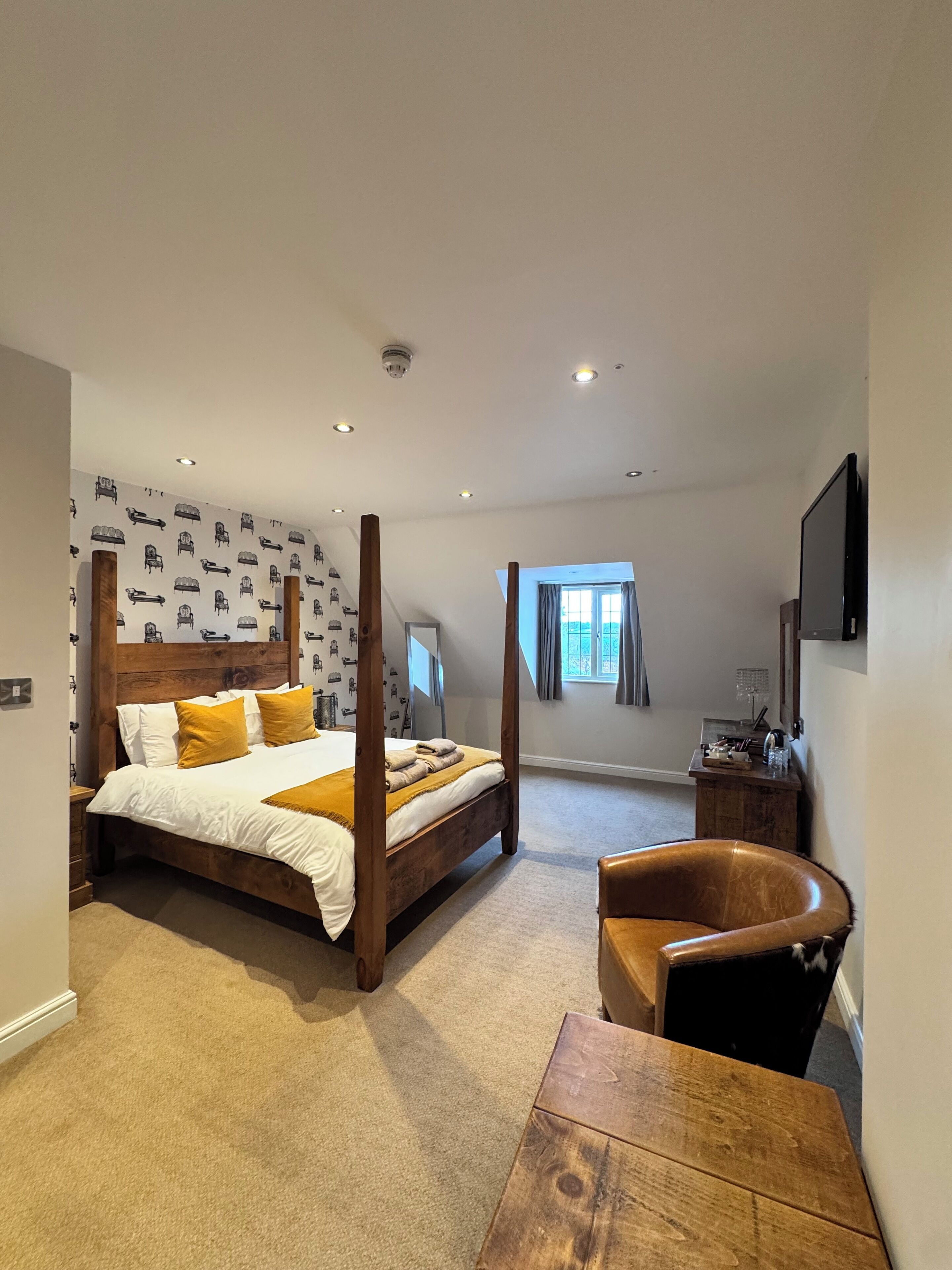 A bedroom with a four-poster bed, a wooden desk, a chair, a TV, and a window with curtains.