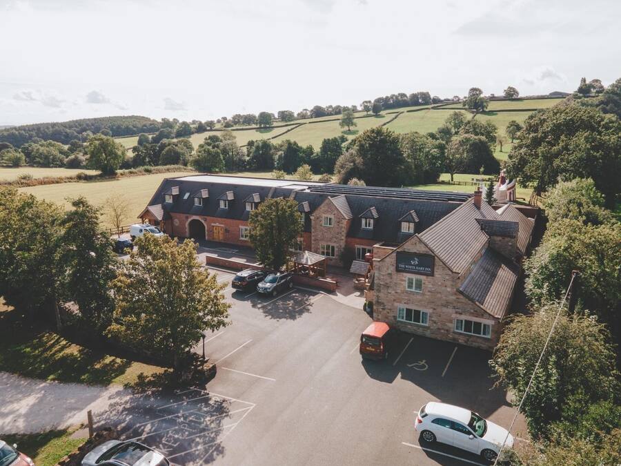 Un grand immeuble à étages, doté d’une façade en pierre, d’un parking et offrant une vue pittoresque sur la campagne environnante.