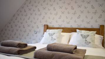 A neatly made bed with folded towels, a wooden headboard, and butterfly-patterned wallpaper.