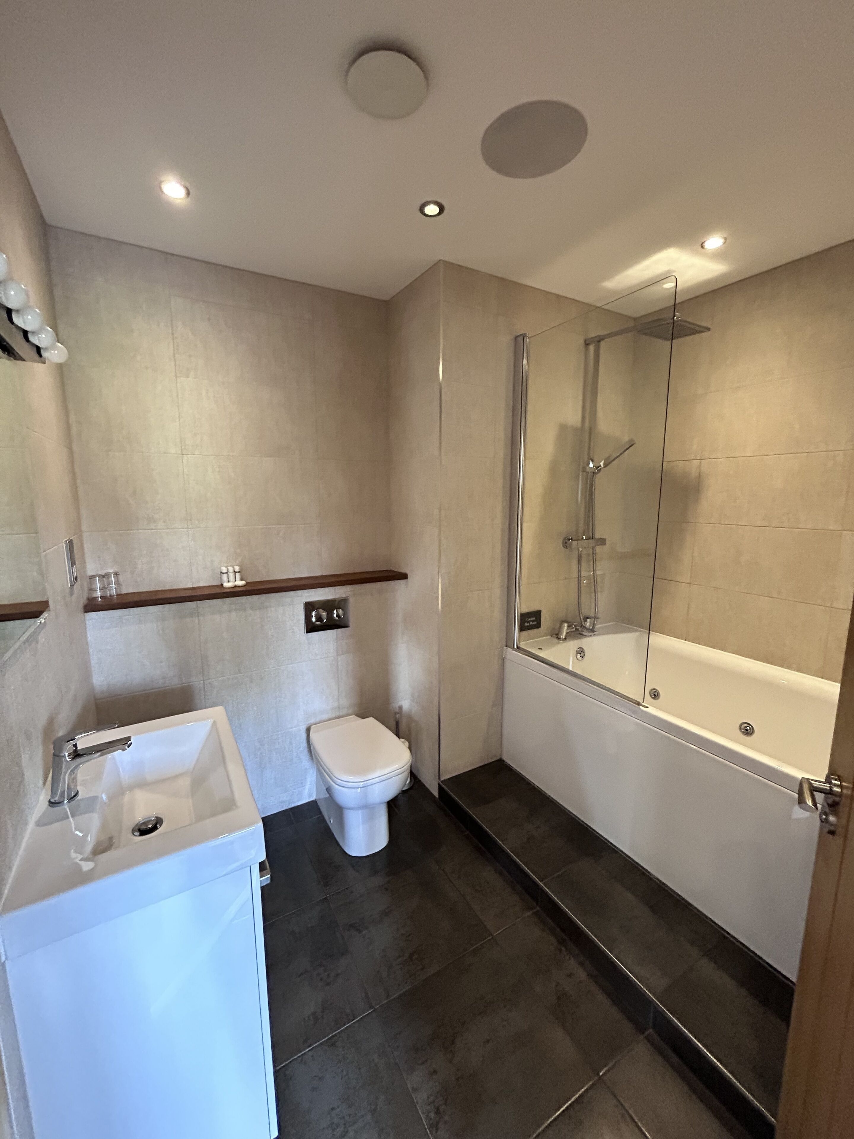 Een moderne badkamer met een douche met glazen wand, een wit wastafeltje en een toilet.