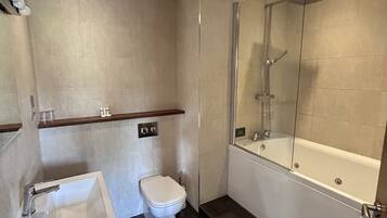 Een moderne badkamer met een douche met glazen wand, een wit wastafeltje en een toilet.