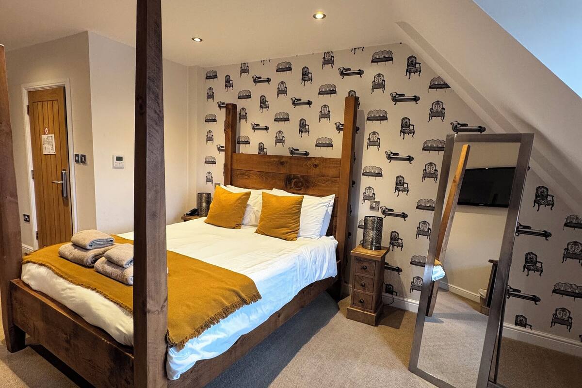 Quarto com cama de dossel, cabeceira de madeira e papel de parede estampado.