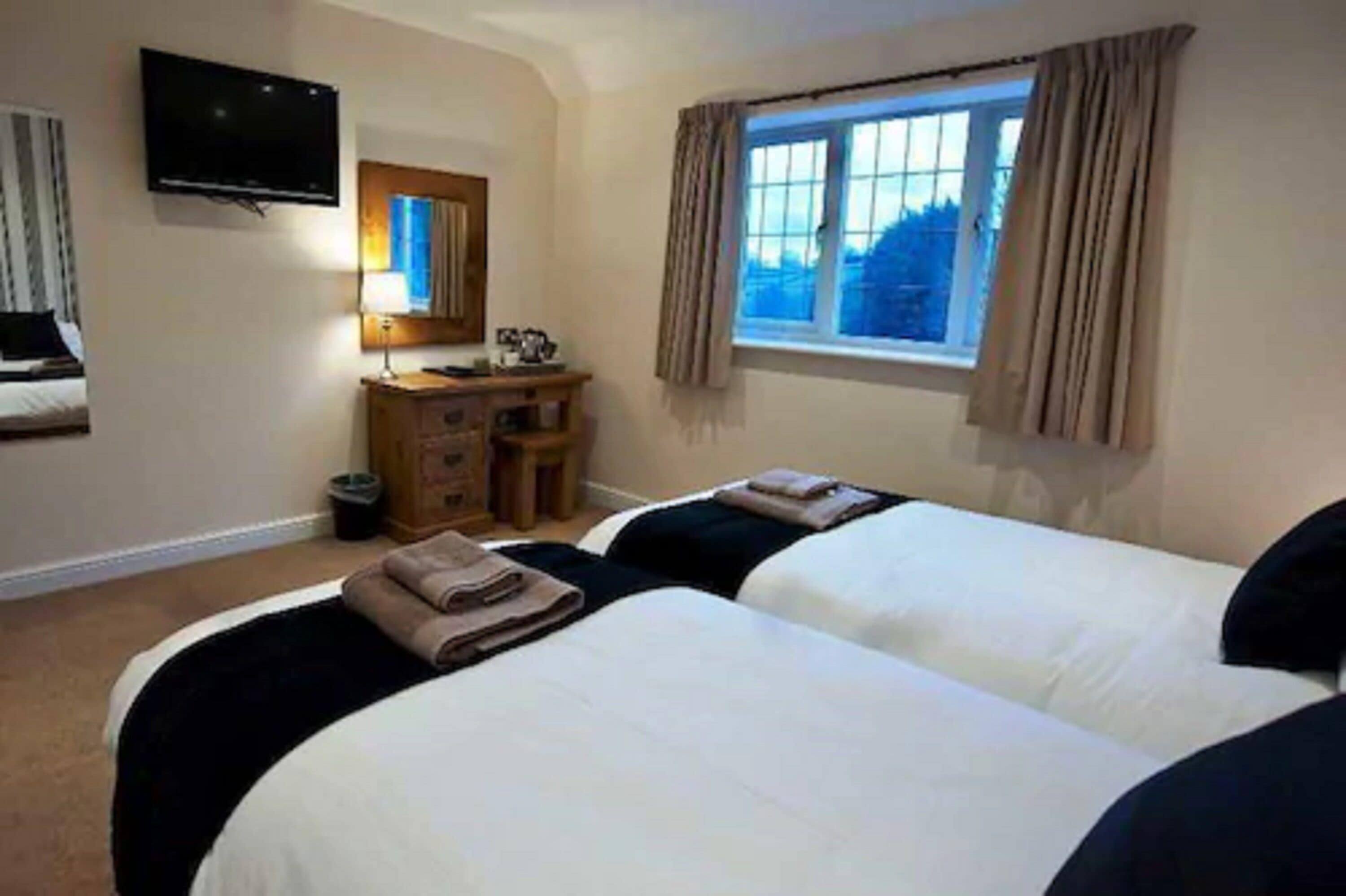 Habitación de hotel con dos camas, televisión, escritorio con lámpara y ventana con cortinas.