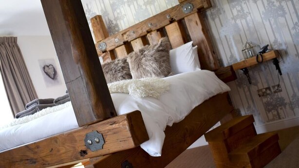 A rustic wooden bed with a headboard, white bedding, and a fluffy white throw. - White Hart Inn (Alfreton)