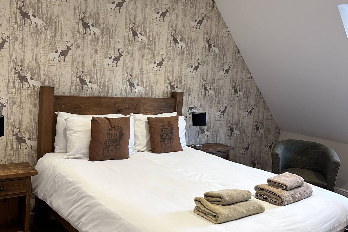 Quarto com cama de madeira, roupa de cama branca e papel de parede com tema de veado.