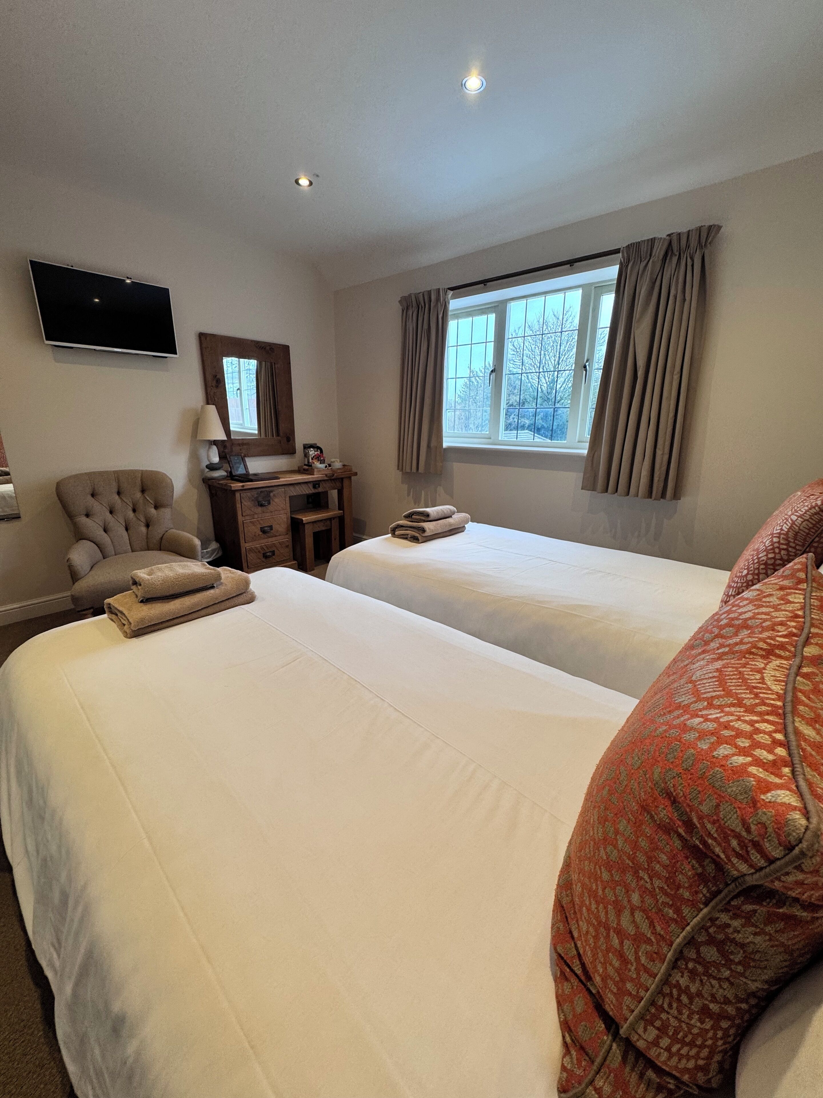 Habitación de hotel con dos camas, televisión, escritorio con lámpara y ventana con cortinas.